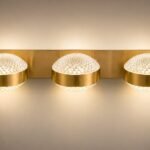 Modern brushed brass 3-light wall sconce featuring round diamond-cut textured crystal glass globes emitting a warm illuminated glow.
