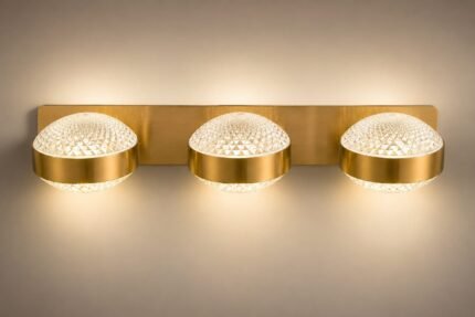 Modern brushed brass 3-light wall sconce featuring round diamond-cut textured crystal glass globes emitting a warm illuminated glow.